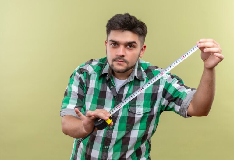 young-handsome-guy-wearing-checkered-shirt-holding-measurer-standing-khaki-wall_141793-30747