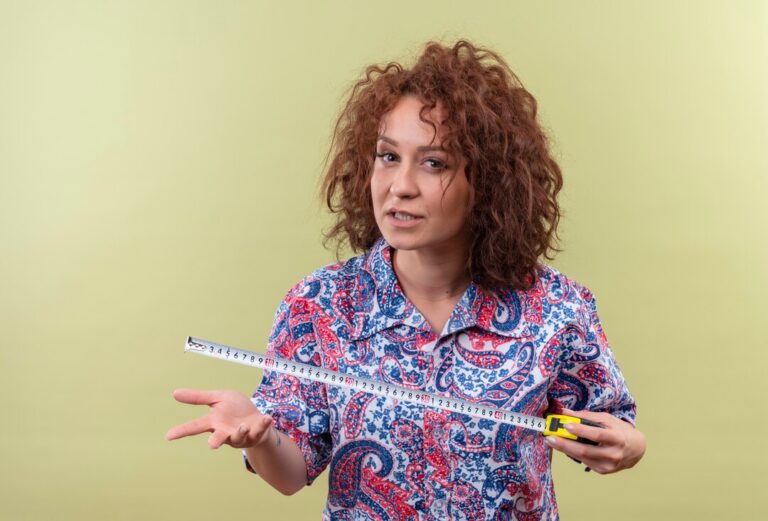 young-woman-with-short-curly-hair-colorful-shirt-using-measure-tape-looking-with-agressive-expression-standing-green-wall_141793-29377